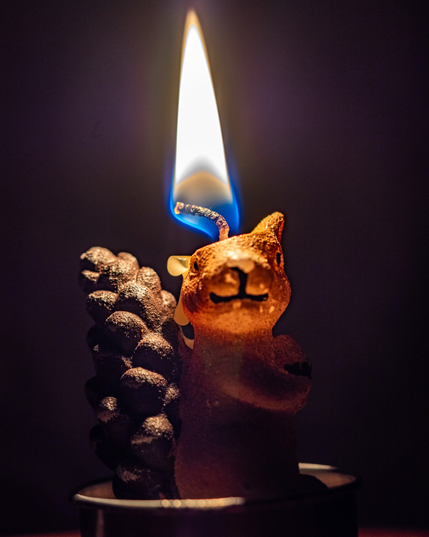 A decorative candle in the shape of squirrel is lit with a warm glow coming from the top of the candle