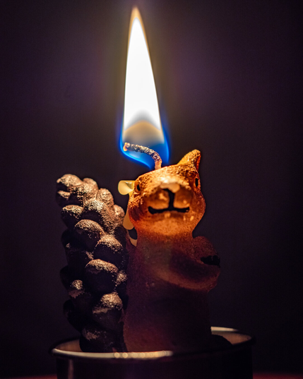 A decorative candle in the shape of squirrel is lit with a warm glow coming from the top of the candle