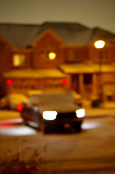Blurry parked cars, head ’n’ red lights, with lit posts, trees and homes on each side, completely still, in light snowy skies and grounds, of that 'Sun'-day night.