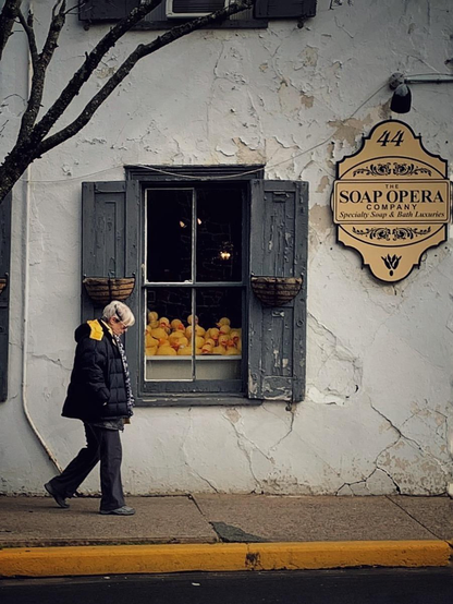 An old woman walks past a window full of yellow rubber ducks.