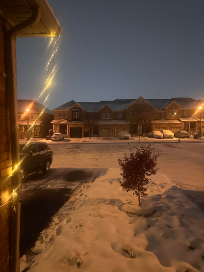A wintery night in a residential area as white blankets the ground and rooftops of the red brick townhouses lining the street.

Cars are covered with parked snow. A red tree stands in a blue tire on the white lawn. 

Yellow lights of lamps, lit strings strung across a porch, invite the blue-light sky to bid its Good Night.