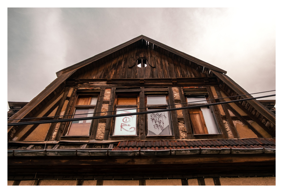 Oberer Teil eines alten Gebäudes mit steilem Dach und Graffiti an den Fenstern; teils verbrettert, teils mit Stoffbahnen bedeckt.