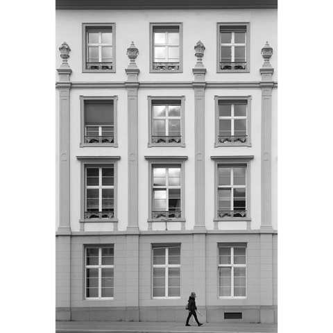 Black and white street photography taken in Luxembourg city. Somebody is walking from left to right before the classic facade of a building of the city center.
