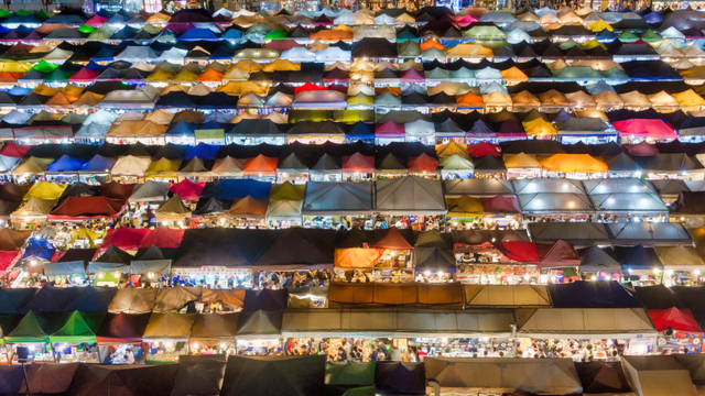 Overhead view of the Train Night Market in Bangkok at night, filled with rows of colorful tents glowing from within, each busy with visitors and vendors.