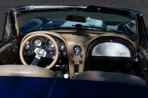 Interior of a dark blue convertible. The dash and steer wheel are wrapped in light tan leather. Chrome highlights abound on the dashboard.