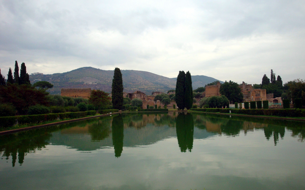A still pond, with ancient buildings beyond.