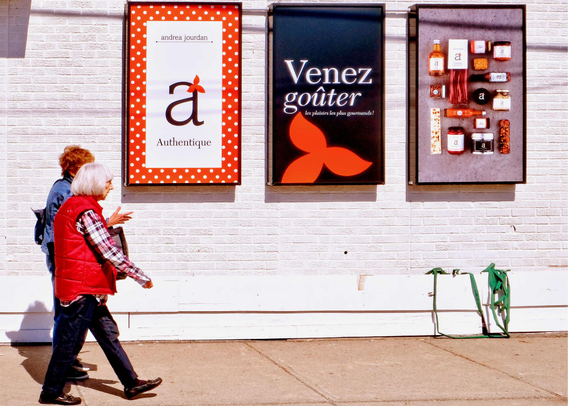 Two women on a city sidewalk walking past 3 advertising posters