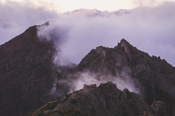Mountains shrouded in fog and clouds after sunset, everything takes on pink and purple hues.