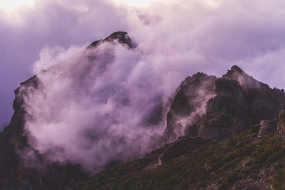 Mountains shrouded in fog and clouds after sunset, everything takes on pink and purple hues.
