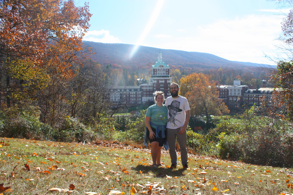 A photo of myself and my husband standing at the crest of a hill. In the background you can see the Omni Hotel and Resort and beyond that is a beautiful mountain range.