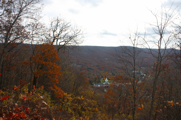 A landscape photo taken from an overlook. Red and orange leaves form a frame around the bottom of the photo. The Omni hotel and resort can be seen in the foreground. Beyond that is the mountain range.