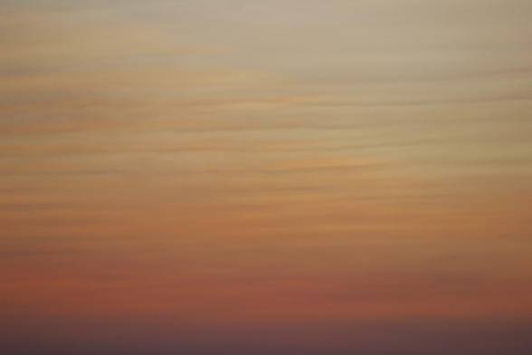 Photograph of horizontally layered clouds at sunset with smoky orange, brown, and grey colors.