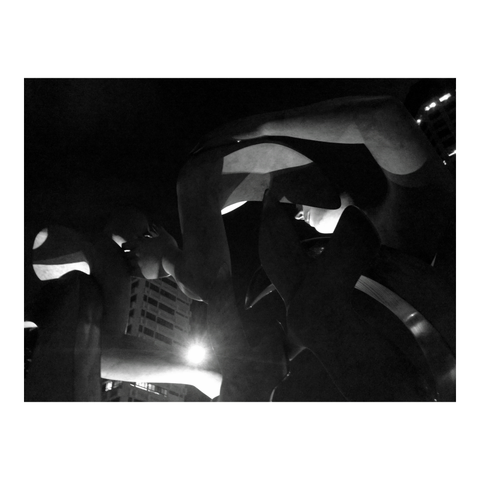 Stone statues and a backdrop of buildings at night. (Version françæ) Statues en pierre et arrière-plan d’immeubles la nuit.