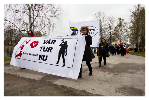 En liggande bild på ett första maj-tåg. Två kvinnor går först med en banderoll med texten ”VÅR TUR NU UNG VÄNSTER”. 