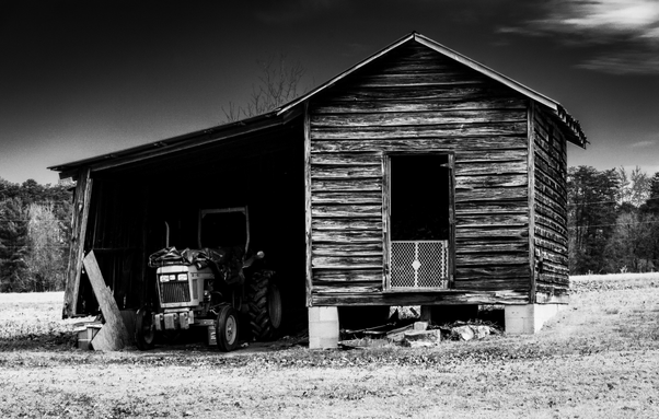 A black and white photo of a wooden tractor barn with a tractor underneath.