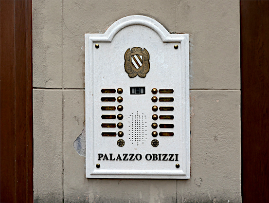 Foto van twee rijen deurbellen met naambordjes onder een wapen gevat in een stenen plaat