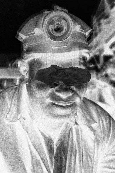 A piece that is part of a series of artworks called 49ers. It's a 3D animation of a rock resembling coal floating in front of a black-and-white negative photographic portrait of an American coal miner from the last century, with a blur effect and light trails around the eyes.
