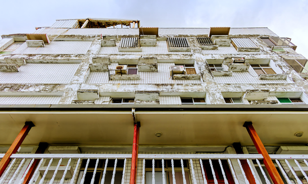 Frog’s-eye view of a facade with a balcony at the bottom and what looks like an abandoned attempt at renovations above.