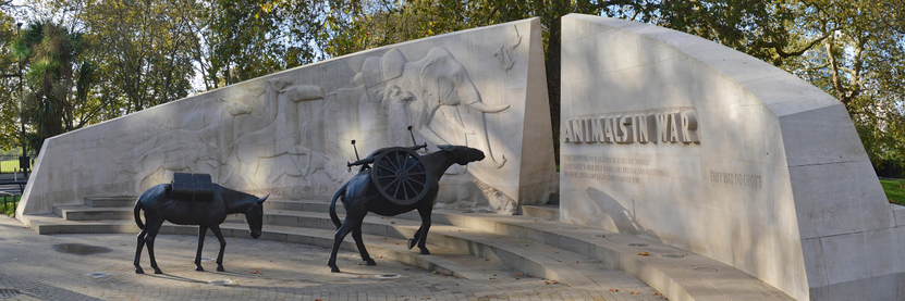 A photo of the front of the Animals in War memorial in London, England. Two bronze sculptures of mules walk toward the gap in the memorial.