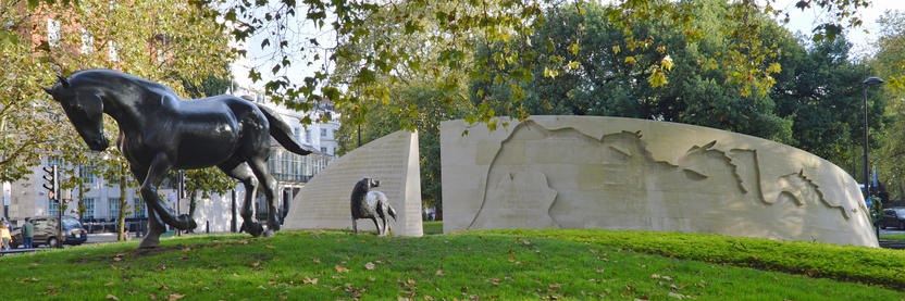 A photo of the back of Animals in War memorial in London, England. A bronze sculpture of a horse and a dog walk away from the gap in the memorial. The sculpture of the dog is looking back at it.