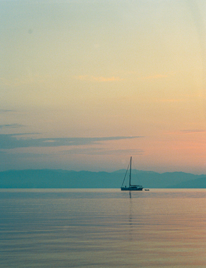 A lone boat at sea at sunrise, with mountains visible in the background.