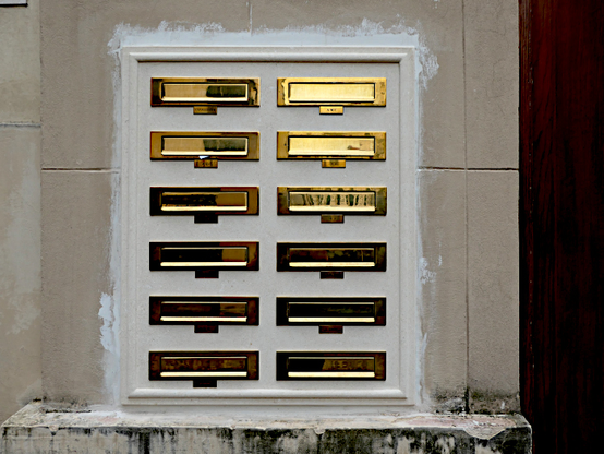 Foto van twee rijen messing brievenbussen in muur