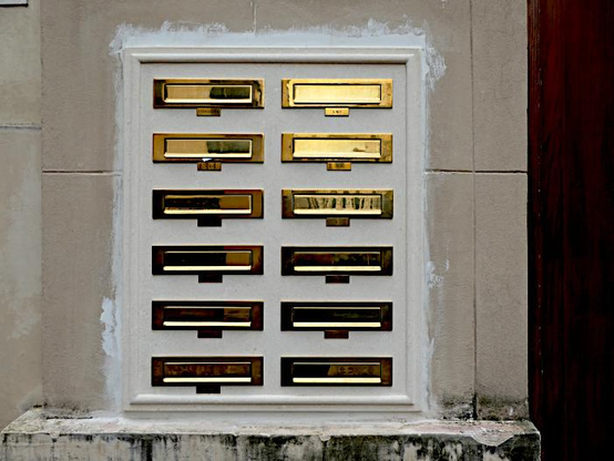 Foto van twee rijen messing brievenbussen in muur