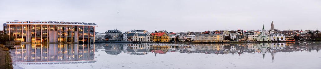 A long picture showing many houses that stand by the tarn in centre of Reykjavík. The tarn is frozen but started to melt so the water on the surface of the ice creates a perfect mirror where all the houses are reflected.