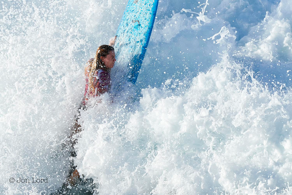 This is a close-up colour sports photo in landscape format of a young female surfer battling with the surf of a large breaking wave. Hermosa Beach, California (2016).

The entire image is filled with a mass of brilliant white foaming surf that's lit by the still low and rising morning sun. To the immediate left of centre is a young woman clinging to her light blue surfboard that's nearly vertical in the water, say sixty or seventy degrees from the horizontal. The front of the board is out of view beyond the upper margin of the image, as is the rear at the base of the photo. Our intrepid surfer is lying prone on the board with her left hand raised and gripping the edge with her hand. She has long blond hair, eyes firmly closed, very, very wet hair, is wearing a red and white top that is partially obscured by spray. Most of her body below the waist is covered by the breaking surf.
After this little argument with the not so pacific, Pacific - she was off again paddling to catch the next wave.