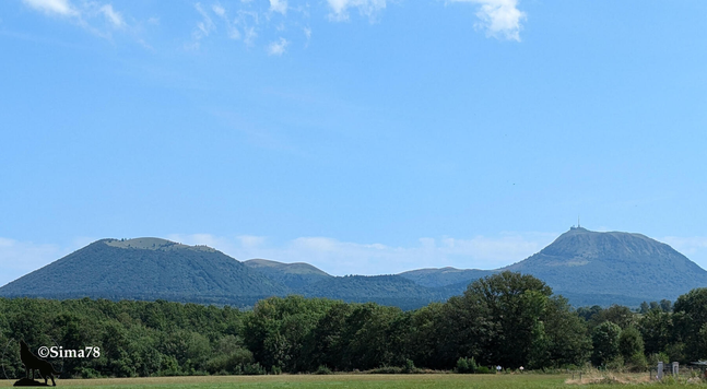 Derrière une ligne de forêt l’on voit les volcans sous un ciel bleu peu nuageux.
Behind a line of forest, you can see the volcanoes under a slightly cloudy blue sky
Detrás de una línea de bosque se ven los volcanes bajo un cielo azul con pocas nubes.