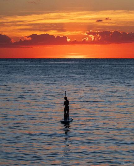 A woman on a Paddleboard is silhouetted at sunset. 
