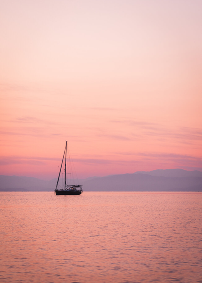 A lone boat at sea during sunrise, there are mountains in the background. The water is really calm.