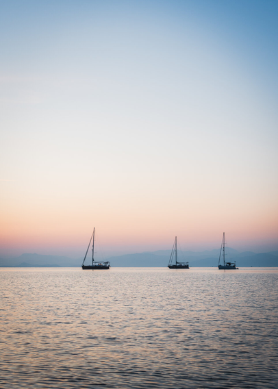 Three boats at sea at sunrise, in the background there are mountains.