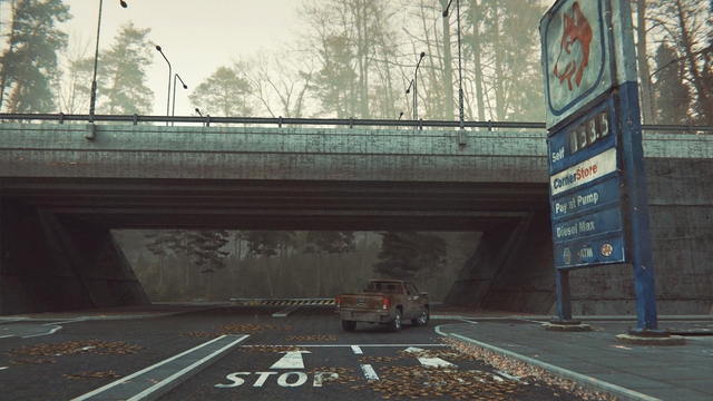 A highway overpass crosses a local road with a gas-station on the right corner. A red pickup truck turns right onto the highway on ramp.  It's late fall, and leaves gather in clumps on the road.