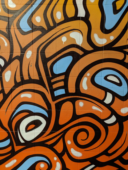 English: Image displays a graffiti mural on a wall outside a rail station in Sydney. The image has orange swirls outlined with black, and a few baby blue highlights. 

Deutsch: Das Bild zeigt ein Graffiti-Wandbild an einer Außenwand eines Bahnhofs in Sydney. Es besteht aus orangefarbenen, schwarz umrandeten Wirbeln und einigen hellblauen Akzenten.

Español: La imagen muestra un mural de grafiti en una pared exterior de una estación de tren en Sídney. La imagen tiene espirales naranjas delineadas en negro y algunos detalles en azul celeste.

Français : L’image montre une fresque de graffiti sur un mur extérieur d’une gare de Sydney. L’image présente des volutes orange cernées de noir et quelques touches de bleu clair.

Türkçe: Görselde, Sidney'deki bir tren istasyonunun dışındaki bir duvarda bulunan bir grafiti resmi yer alıyor. Görselde, siyahla çevrelenmiş turuncu girdaplar ve birkaç bebek mavisi vurgu bulunuyor.

تُظهر الصورة جدارية جرافيتي على جدار خارج محطة قطار في سيدني. تتخلل الص