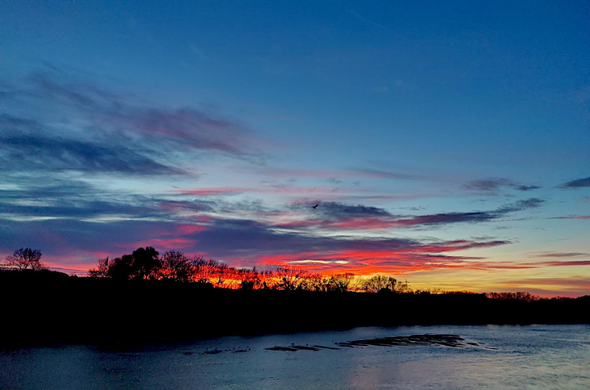 A l'horizon, dessinée par la berge encore sombre du fleuve La Dive proche de l'embouchure et à marée haute, naissent les premières lueurs du jour dans un ciel partiellement dégagé.