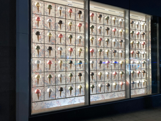 A backlit show window feature many multi-colored ice cream cones.