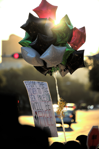 A shot of Palestine-colored balloons during golden hour. The bundle of balloons is backed by the sun peaking through a gap.