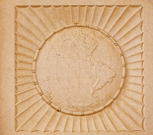 On a light yellowed white background rock is carved an image of the globe centering north America surrounded by what looks like a circle of long beats and outside that a set of scalloped ridges inscribed in a square