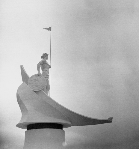 In the black-and-white photo, the monumental sculpture "Onego" on the shore of Lake Onego (a young man with a spear and a shield in a boat) is depicted against a gloomy sky.