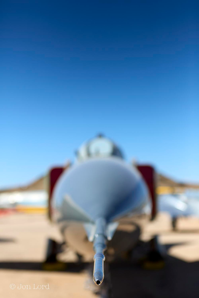 This is an abstract colour photo of the nose of a cold war Soviet MiG-23 fighter jet. Tucson, Arizona (2013).

At the base and in the centre of the image is a narrow, hollow, shiny, metal tube that extends back about a quarter of a metre and gradually blurs out of focus. Beyond is a large, round, nose cone. Behind and blurring further are two rectangular, in the vertical plane, air-intakes both with red blanks inserted. Above is the semi-circle of the canopy with a egg shaped metal frame facing forward. The inboard section of the wings are so blurred it's more left to the imagination. Below the jet is a yellow sandy surface, above, is a clear and cloudless blue sky, graduating darker towards the top of the photo.