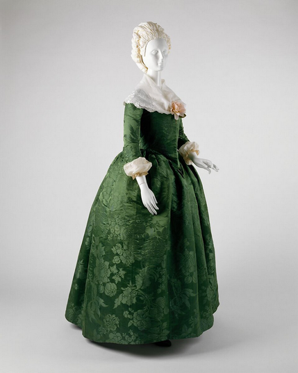 an emerald green floor-length hooped dress on a mannequin, the sleeved coming down to mid-forearm with light fabric on them, a large light kerchief around her shoulders 