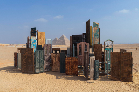 a collection of carved portraits on doors by Vhils installed in the desert near the Pyramids of Giza
