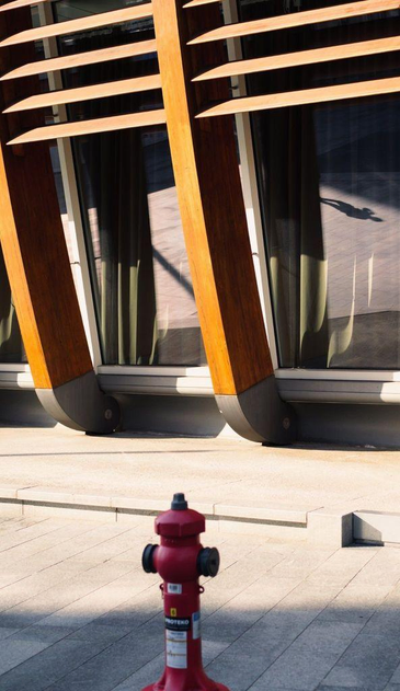 A modern building with large, curved wooden columns and large glass windows. In one of the windows is a reflection of the shadow of a man.