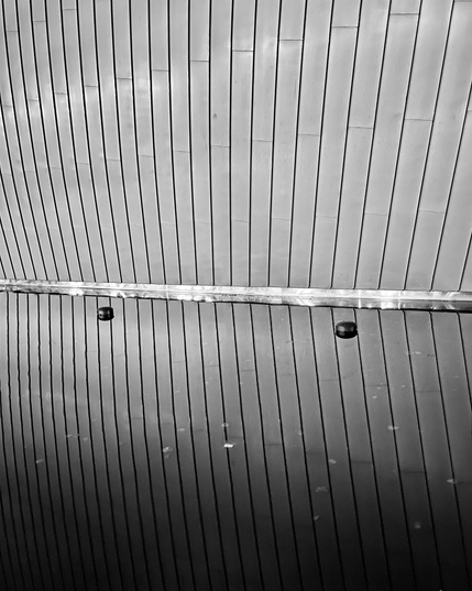 A grayscale image of the vertical wall panels of Kiasma art museum reflecting from a pool of water.