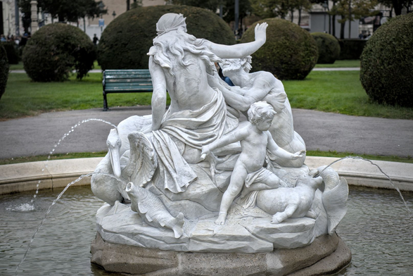 Dieses Foto zeigt einen der Tritonen- und Najadenbrunnen im Maria-Theresien-Park in Wien. Die Skulptur besteht aus Carrara Marmor.

Im Zentrum sitzt eine Najade (eine weibliche Wassernymphe), die sich nach hinten lehnt und einen Arm ausstreckt.
Neben ihr befindet sich ein Triton (ein männlicher Meeresgott), der sich dynamisch nach vorne beugt.
Ein kleiner Knabe sitzt auf einem Seehund.
Um die Figuren herum spritzt Wasser aus den Mündern der Tierwesen, was dem Brunnen eine lebendige Atmosphäre verleiht.

Der Brunnen ist aus weißem Marmor gefertigt und wirkt sehr elegant und detailreich.