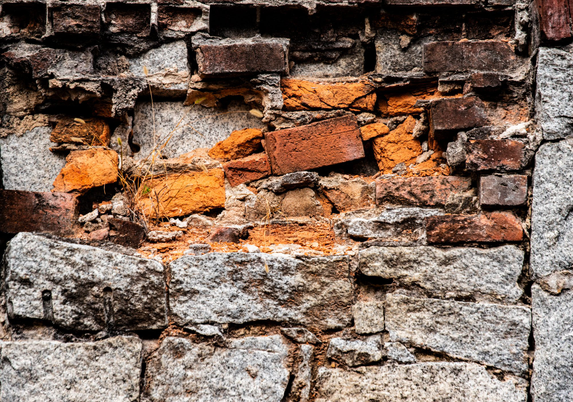 A combination brick and stone wall with some of the bricks randomly placed and many crumbling away.