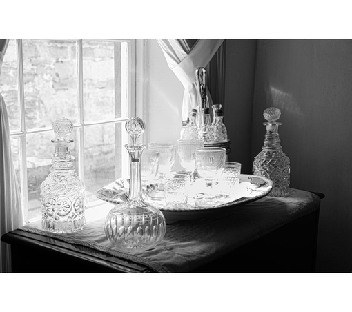 Crystal decanters and glasses are elegantly arranged on a tray by a sunlit window. The scene conveys a vintage, sophisticated atmosphere.
