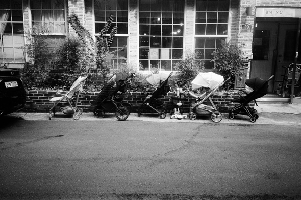 어린이집의 큰 유리창과 화단 앞에 각양각색의 유아차가 나란히 일자로 주차되어 있다.