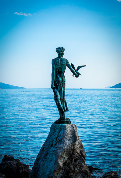 A photograph of a woman statue holding a bird on a rock.